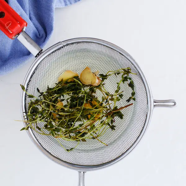 a strainer with thyme and ginger for making homemade cough syrup